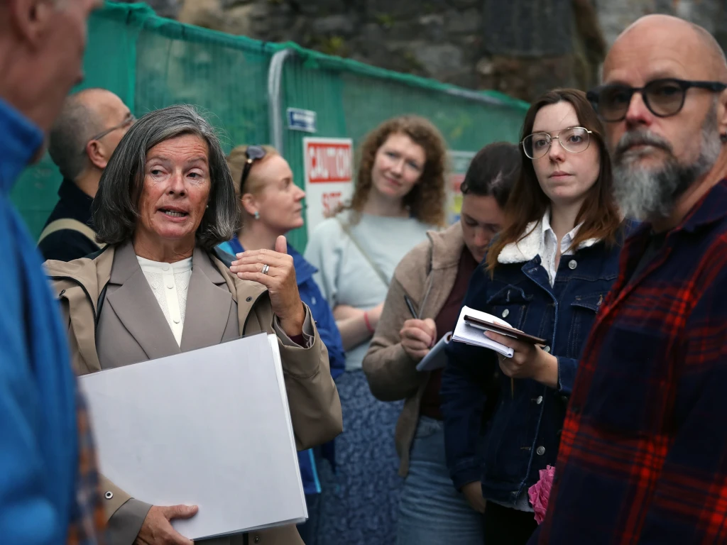 A group of people gathered in front of a fenced-off derelict site.
